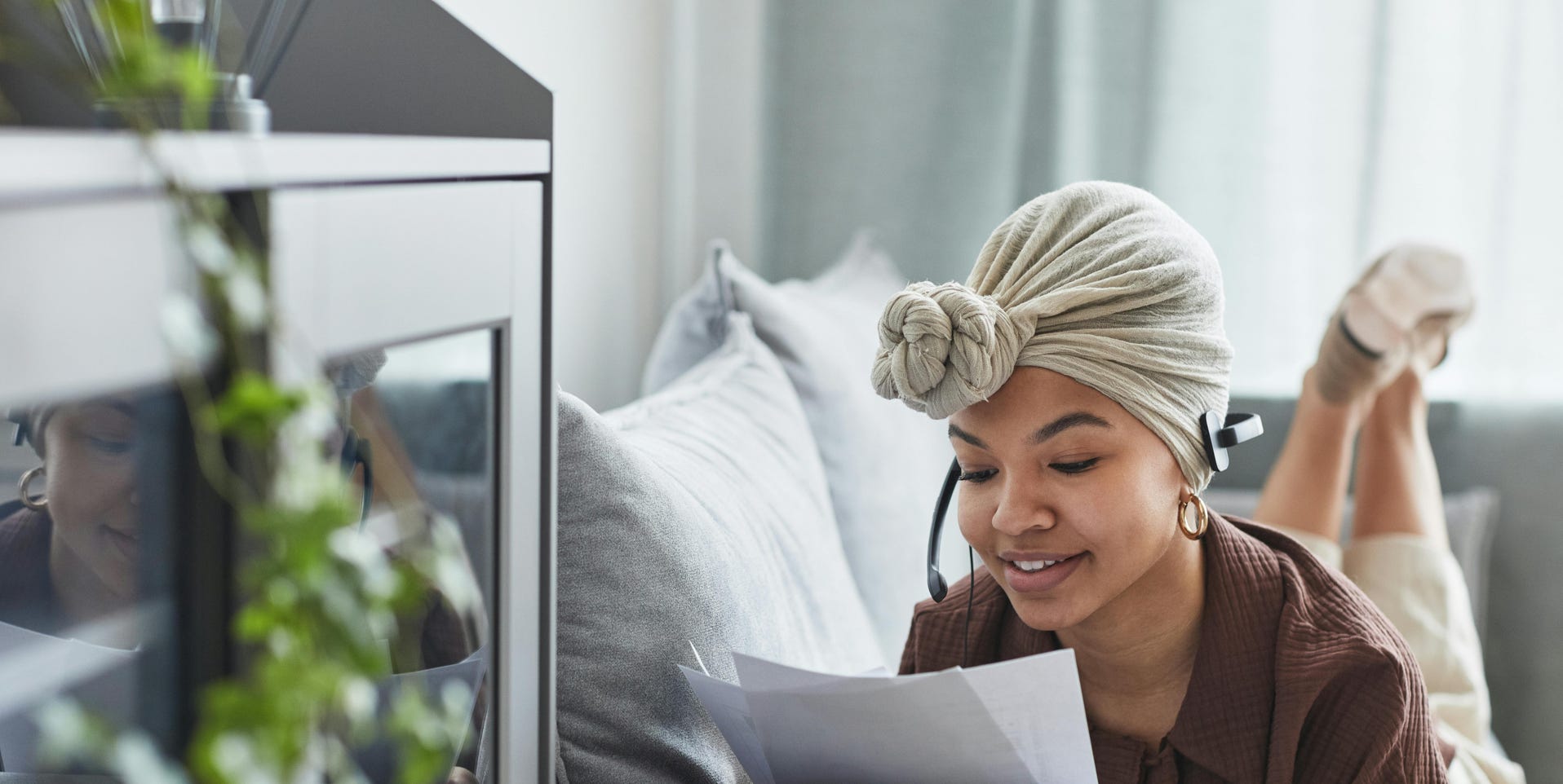 Smiling woman with headset reviewing documents on sofa, working from home.